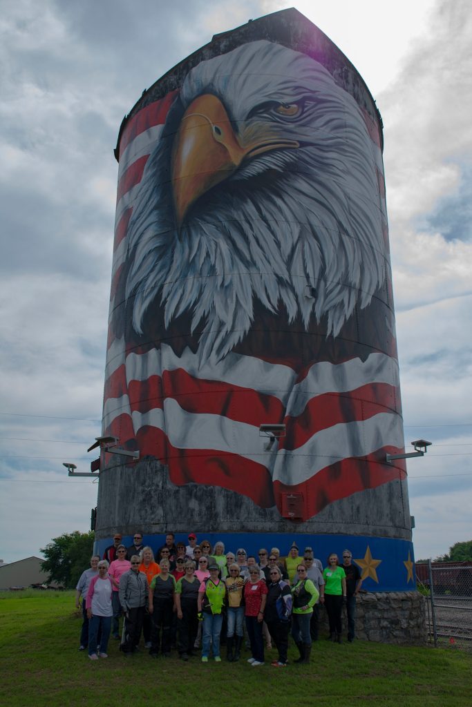 Group standing below a silo painted with an eagle and an American flag