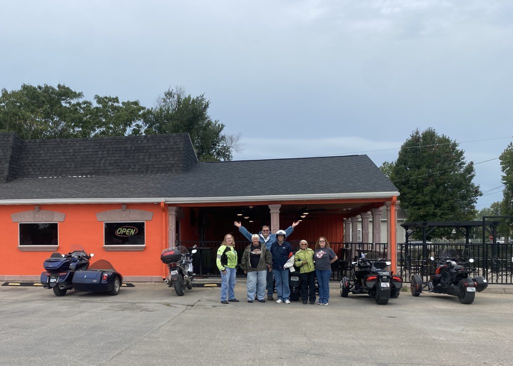 Riders and motorcycles gathered in front of an orange restaurant building