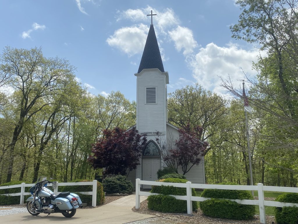 Motorcycle parked in front of a small white church with a steeple
