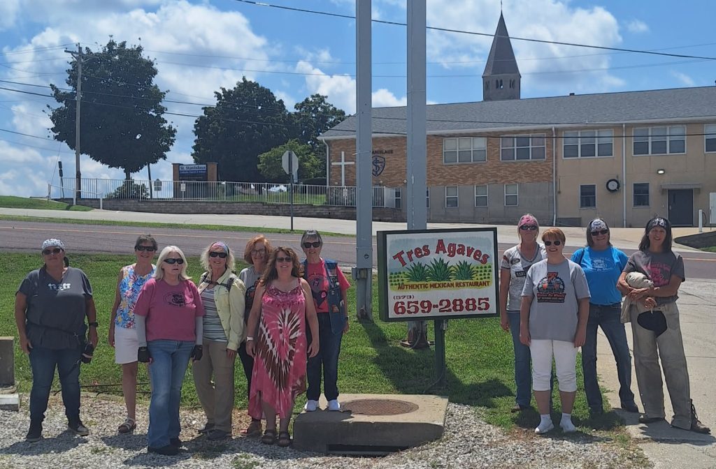Group of riders standing beside a Tres Agaves restaurant sign